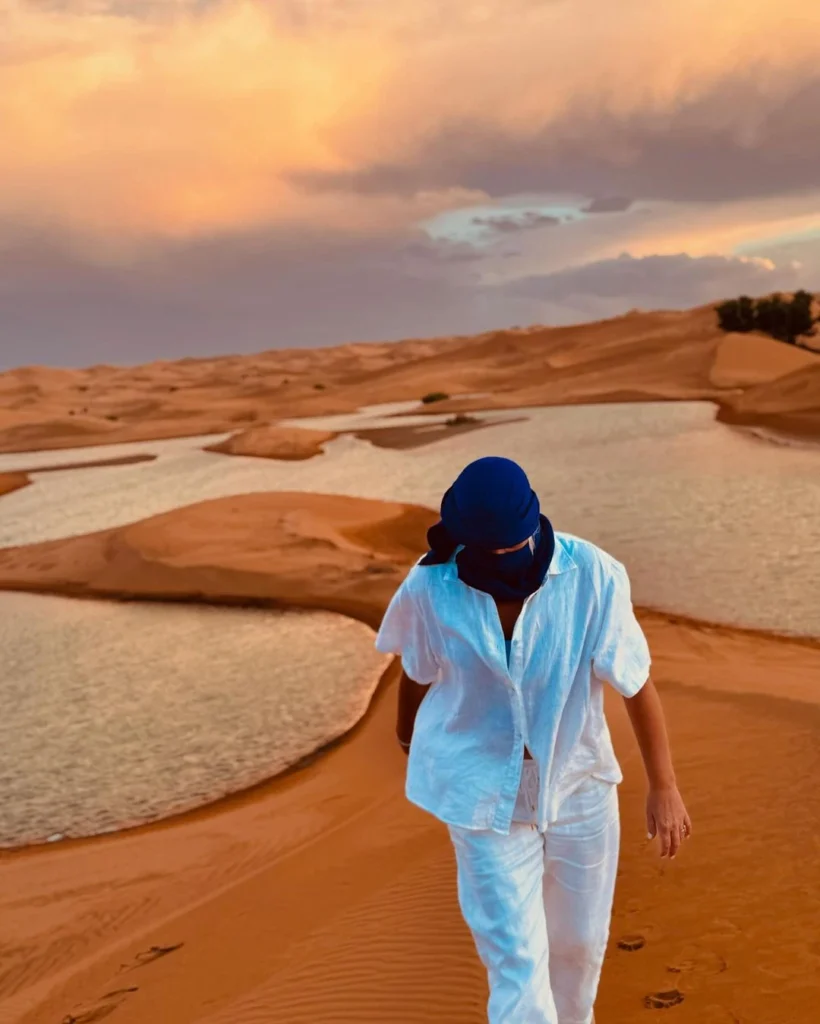 A traveler admires a magical scene that blends the sunset with a lake surrounded by sand dunes.