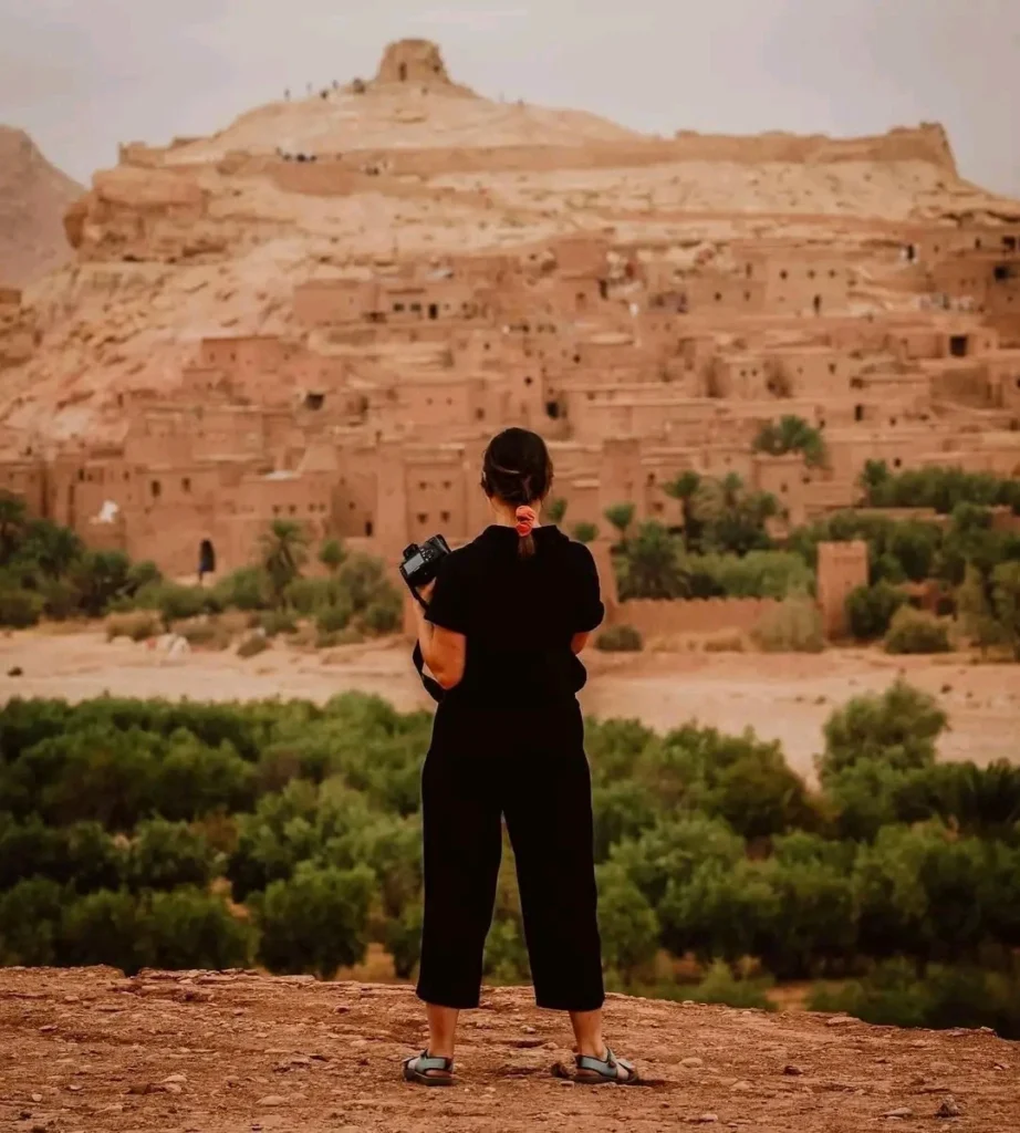 An American tourist admires the breathtaking view of Kasbah Ait Benhaddou from an elevated area during her trip from Marrakech to Sahara Desert.