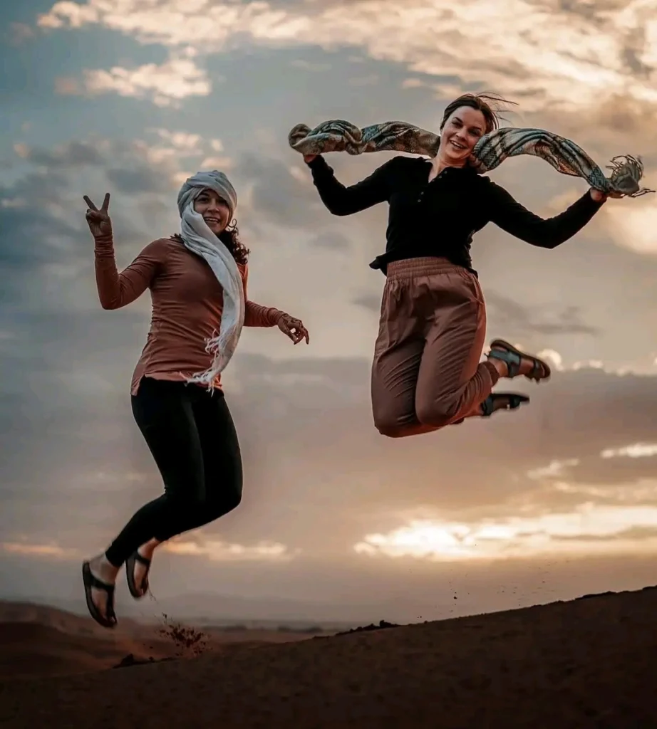 Two girls enjoy jumping over the sand dunes during a 5-day Marrakech to Sahara Desert tour.