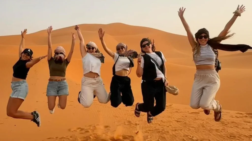 A group of travelers jumping in the air among the sand dunes of Merzouga Desert, expressing excitement and adventure during a one week itinerary in Morocco.