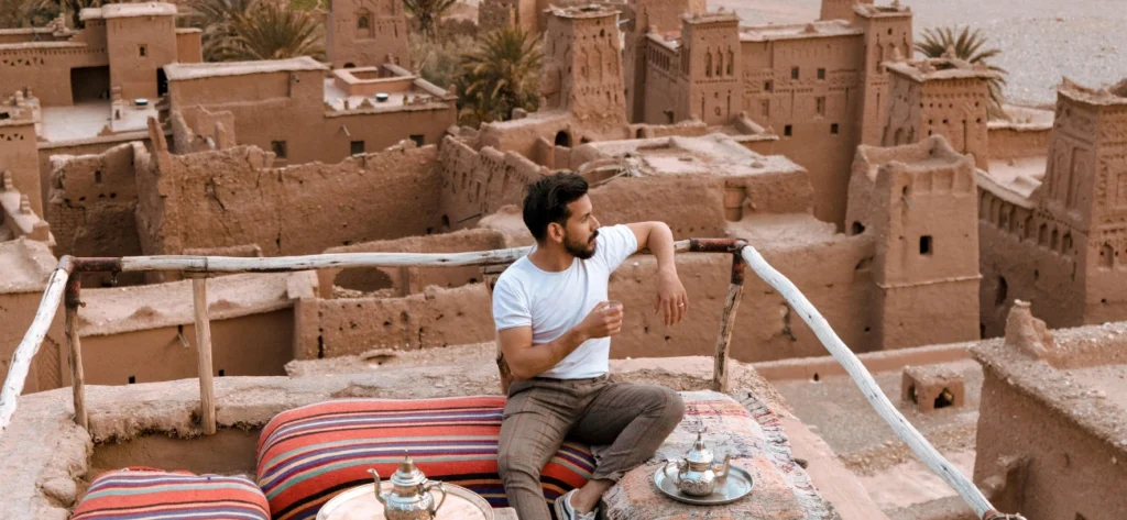 A traveler sitting on the rooftop of Ait Ben Haddou, enjoying tea and the view during a 3 days tour from Marrakech to Fes via Merzouga.