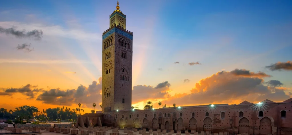 The illuminated minaret of Koutoubia Mosque in Marrakech, glowing at sunset, surrounded by palm trees and historic architecture, captured during a Morocco in 3 days tour.