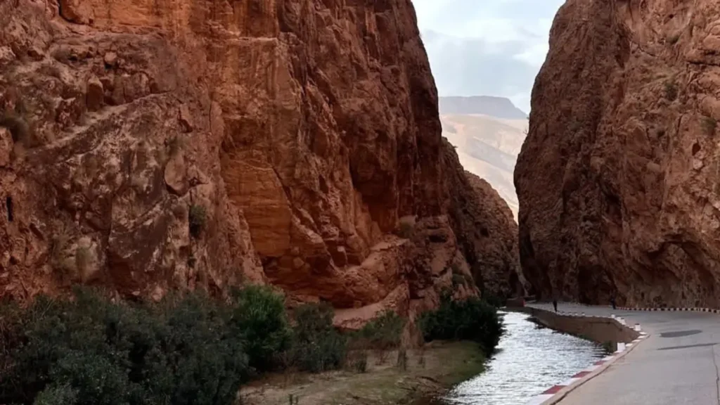 Todra Gorge in Morocco, with towering red rock walls and a calm stream beside a paved path, during a one week itinerary