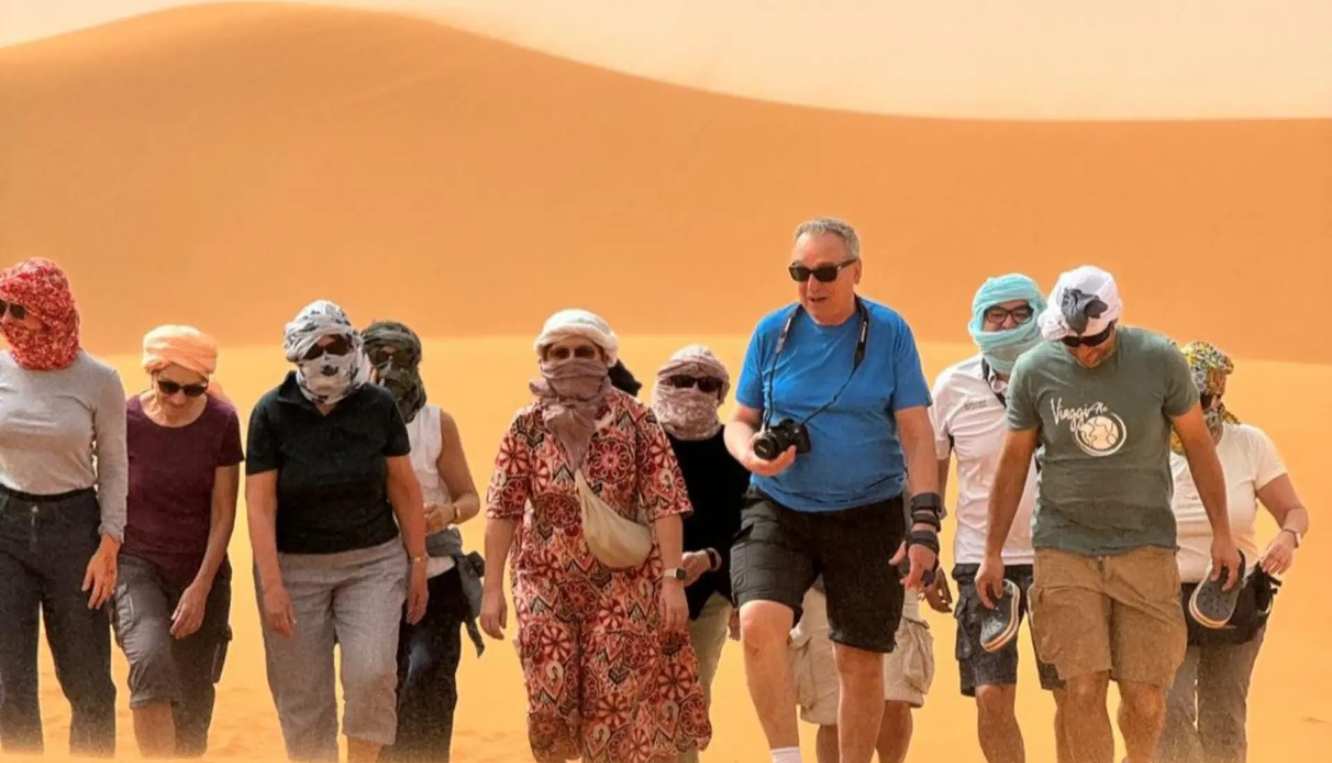 A diverse group of travelers walking on golden sand dunes during a shared 3 days desert tour from Marrakech to the Sahara desert.