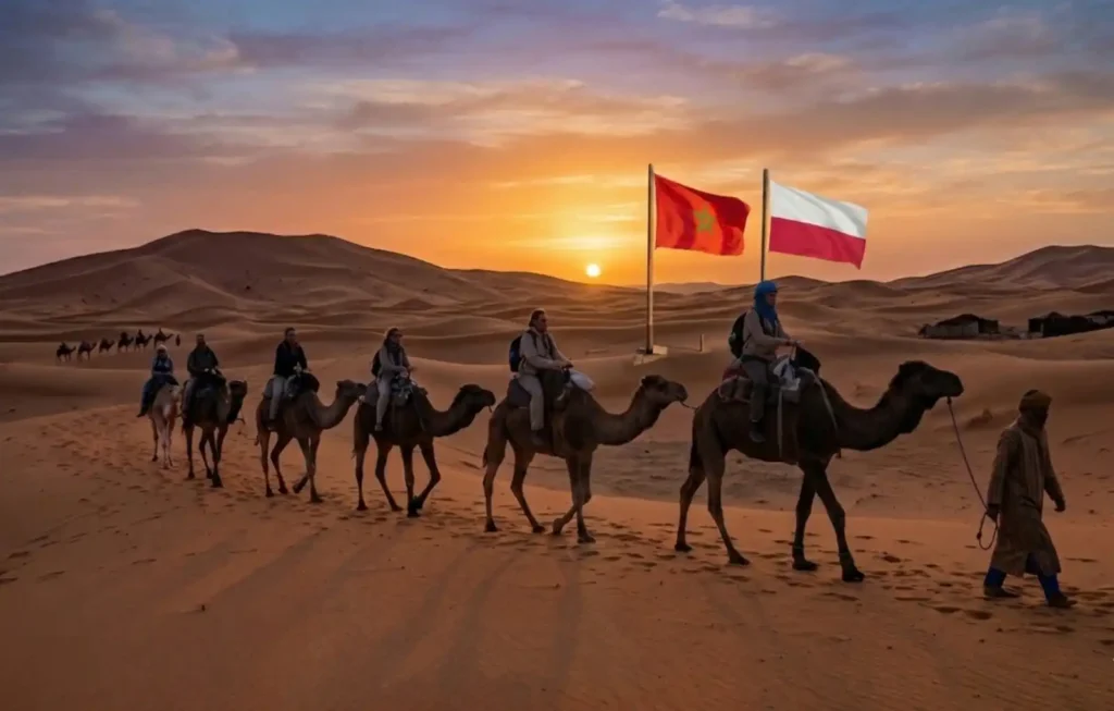 A group of travelers on a camel trek through the Erg Chebbi dunes at sunset, with the flags of Poland and Morocco displayed in the background to welcome tourists looking for Morocco Desert Trips and professional Marrakech Desert Tours.