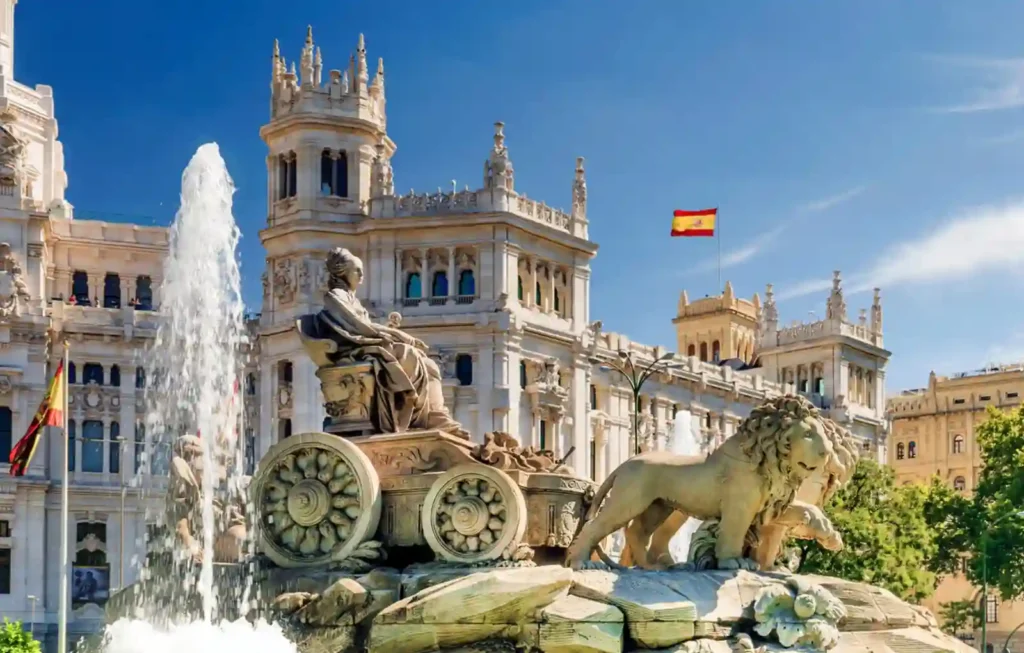 The iconic Cibeles Fountain featuring the goddess Cybele on a chariot and the Cybele Palace (Palacio de Cibeles) under a clear blue sky in Madrid, Spain. This landmark serves as a primary starting point for travelers planning an integrated journey for their travel to Spain Portugal and Morocco.