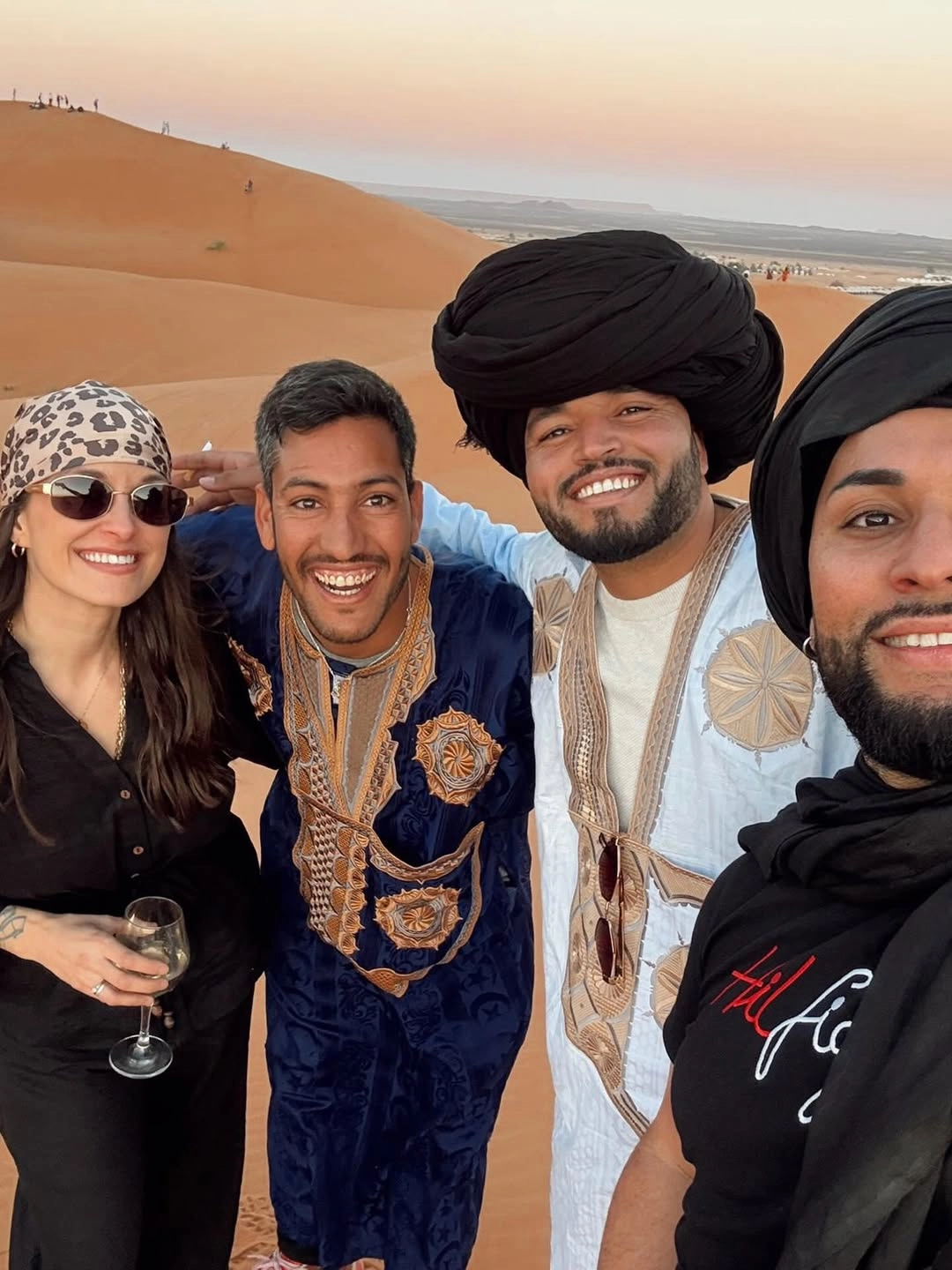 Two travelers from Colombia enjoying sunset in the Merzouga desert with two Moroccan guides during their travel to Morocco from Colombia.