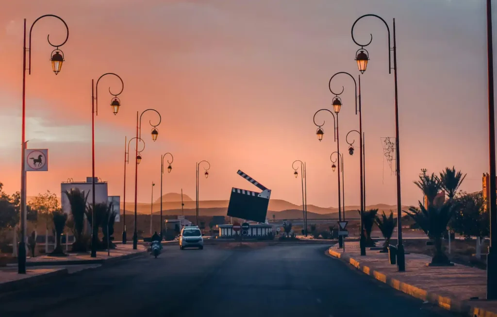A scenic sunset view of the famous giant movie clapperboard monument in Ouarzazate, Morocco. This landmark is a top highlight for those who travel to Morocco from Japan, showcasing the city's role as the "Hollywood of Africa" with its unique street lamps and desert mountain backdrop.