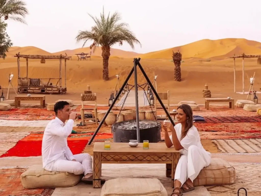 A couple enjoying traditional tea at a luxury desert camp in Merzouga during the best time for a Marrakech desert trip.