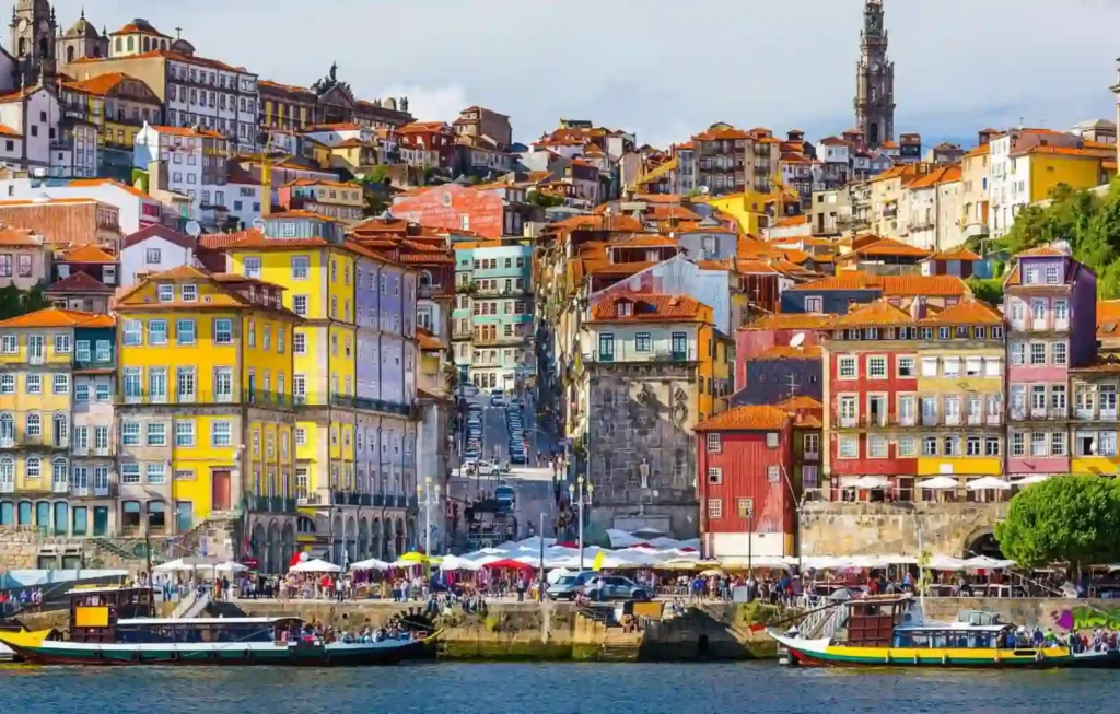 The vibrant and colorful riverside houses of the Ribeira district in Porto, Portugal, overlooking the Douro River with traditional Rabelo boats in the foreground. This iconic Portuguese cityscape represents a key destination for travelers on a combined travel to Spain Portugal and Morocco tour.