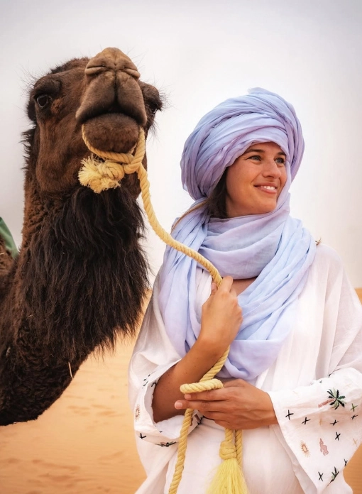 An adult and a young boy from the Moroccan people wearing traditional white djellabas and colorful turbans in a Merzouga shop.