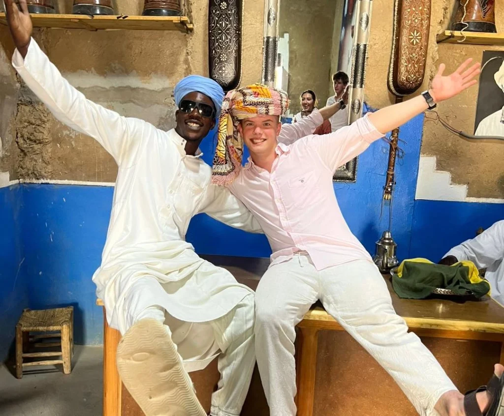 A traveler and a local Black man from the Gnawa community smiling and celebrating together in Khamlia, Morocco.