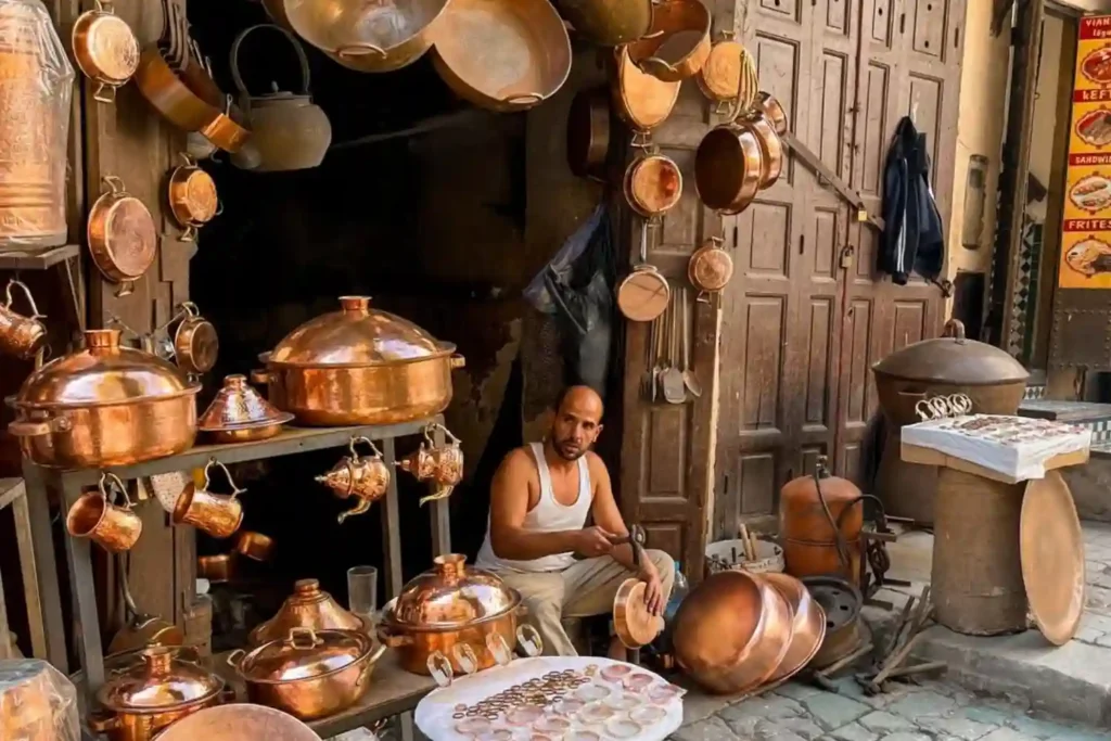 A skilled Moroccan craftsman working with copper and brass pots in a traditional open-air workshop within the Fes Medina, showcasing the authentic and welcoming atmosphere that helps travelers decide if Fes Morocco is safe to visit.