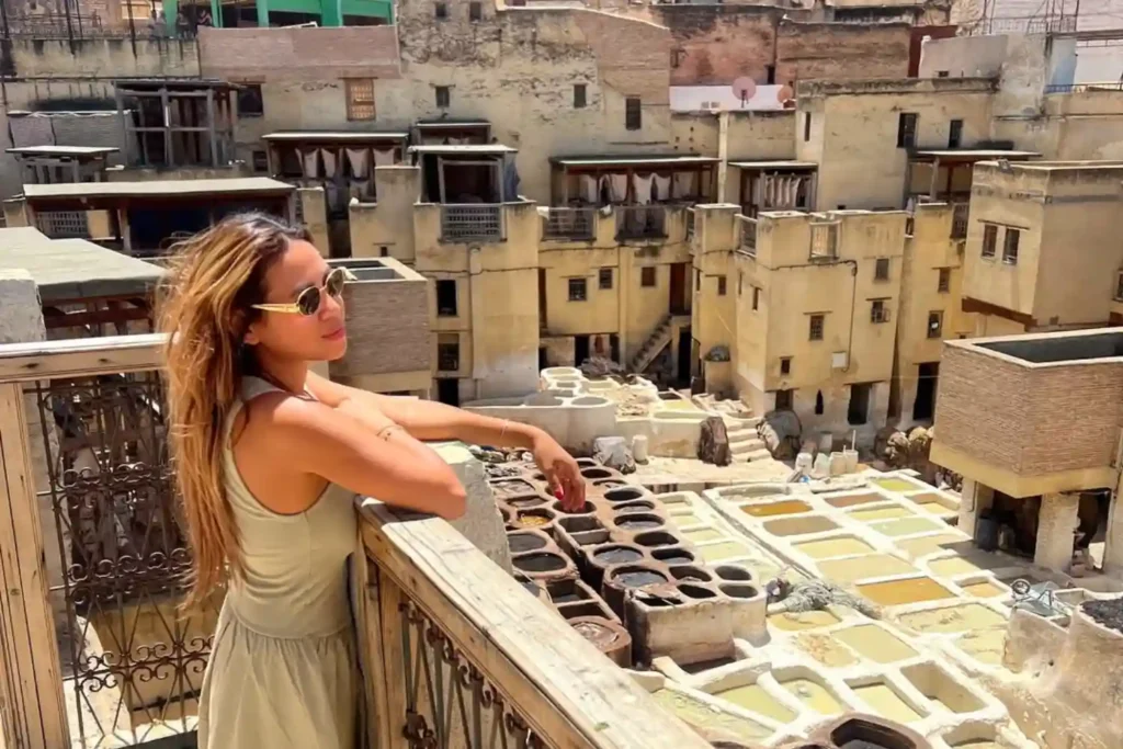 A female traveler with sunglasses leaning on a wooden balcony overlooking the historic Chouara Tannery in Fes, Morocco, illustrating the popular sightseeing spots and whether Fes is safe for international tourists.