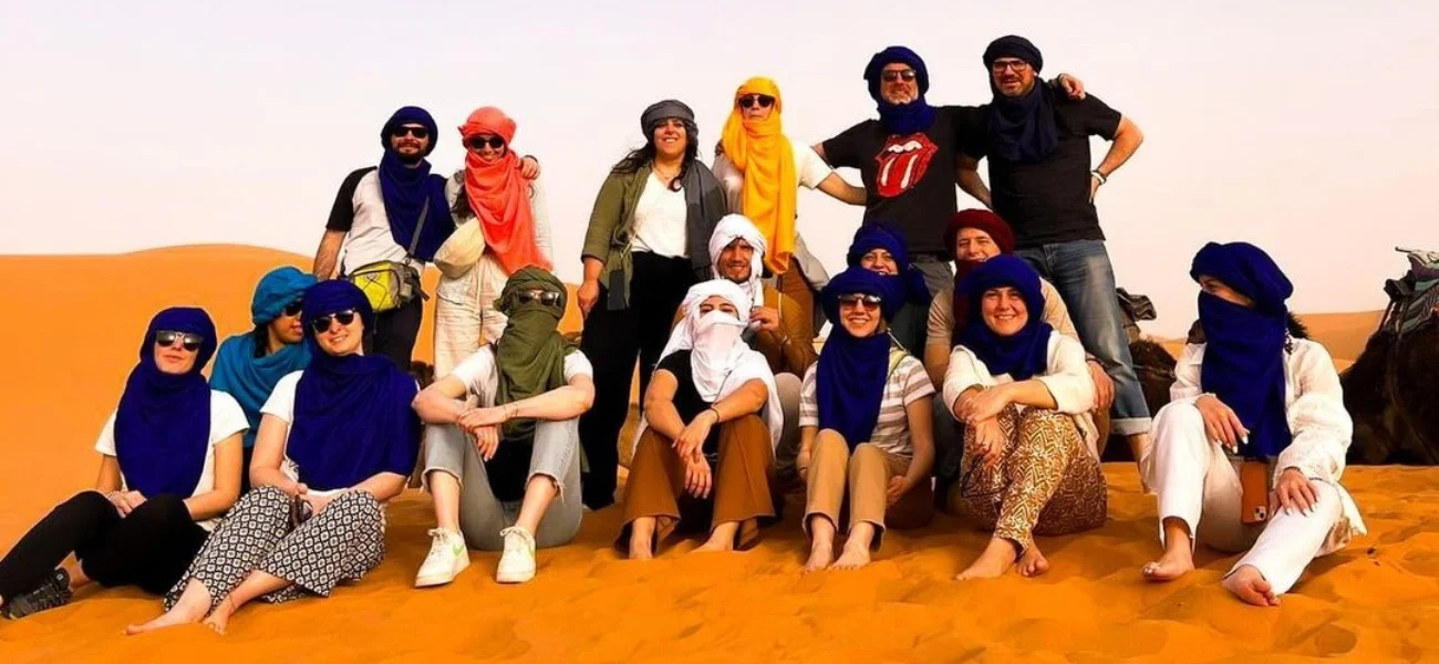 Sixteen travelers posing on a glowing sand dune under a clear sky during their 3 days in Morocco desert experience.